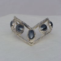 Five fouteen by ten oval Hematite stones bezel set connected by two triangular wires which are formed to a chevron shape. Worn with chevron pointing down